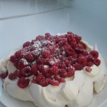 Sieving icing sugar over a pavlova with raspberries Sieving icing sugar over a pavlova with raspberries